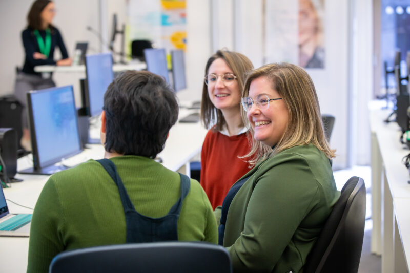 three female trainees smiling at each other in front of computers